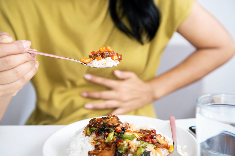 A woman is eating very spicy food that irritates her stomach, so she is clutching her stomach.