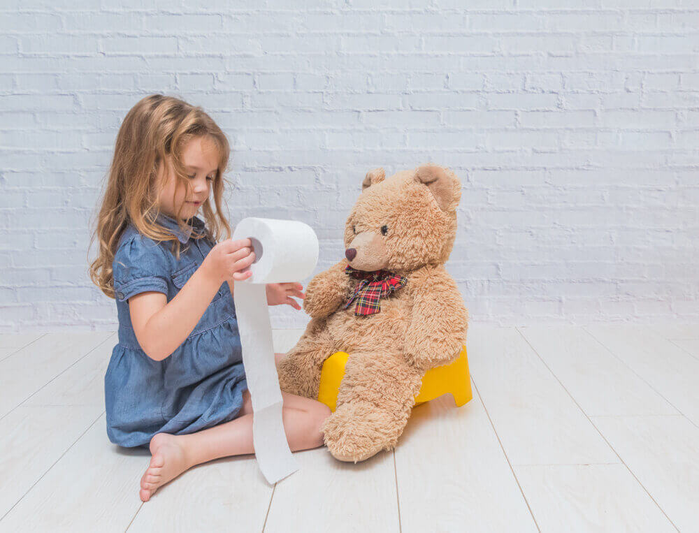 Djevojčica sjedi na podu i igra se rolom toalet papira, a na kahlici pored nje sjedi plišani medvjedić.