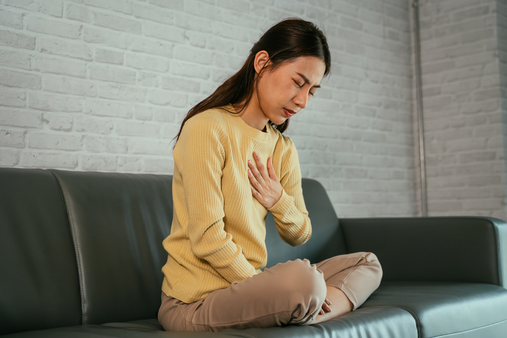 A young woman sits on a green couch and clings to her burning chest.