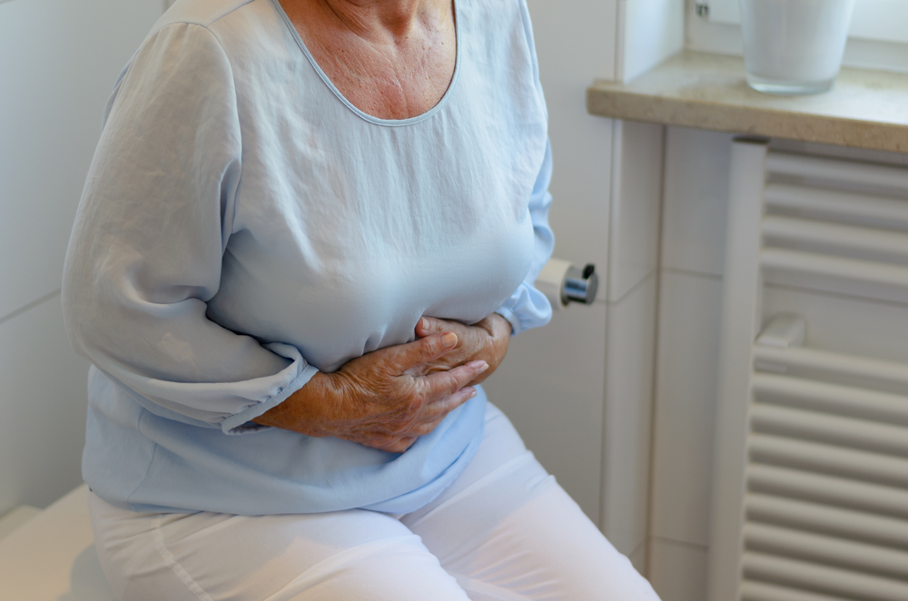 Die Frau sitzt auf der Toilette und klammert sich an ihren Bauch, weil sie verschlossen ist.