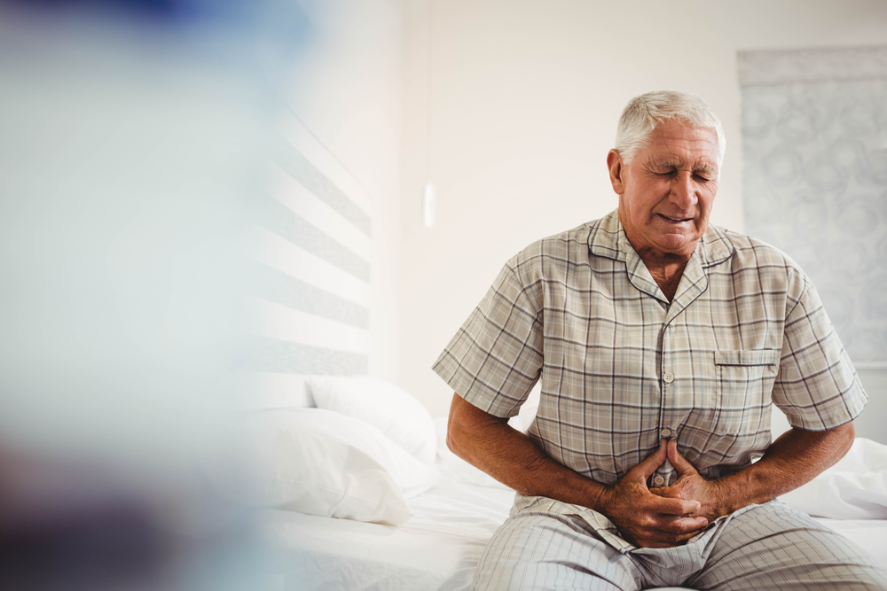 The man sits closed on the bed and holds on to his stomach.