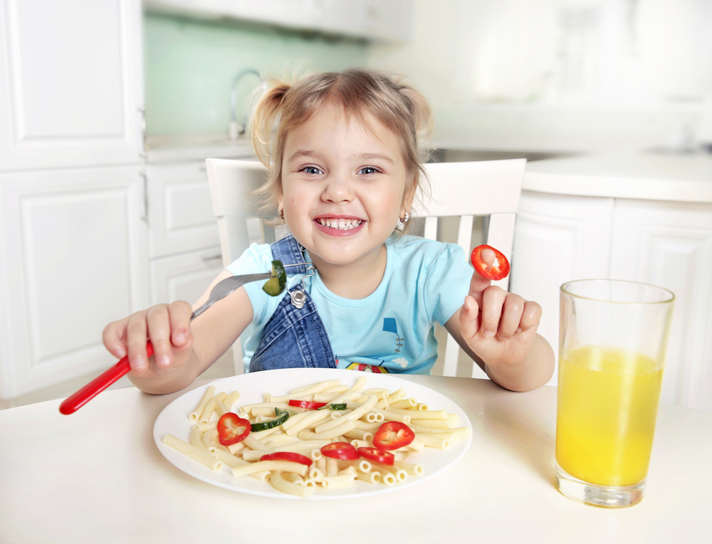 Das kleine Mädchen isst ein gesundes Mittagessen und trinkt daneben Orangensaft.