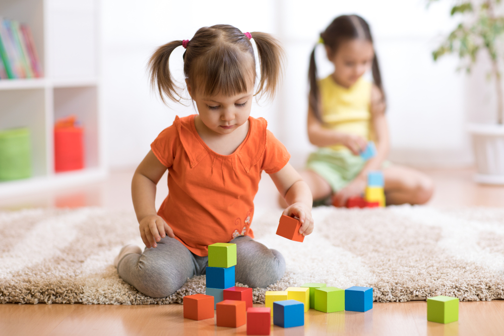 The girls are playing with dice on the carpet in the living room.