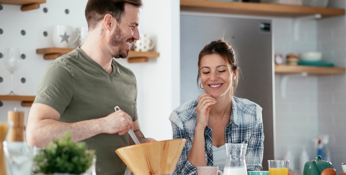 Nasmejana mož in žena skupaj pripravljata zdravo kosilo.