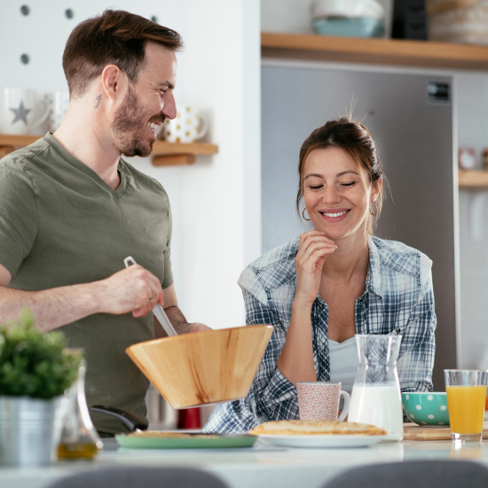 Marito e moglie sorridenti che preparano insieme un pranzo sano.