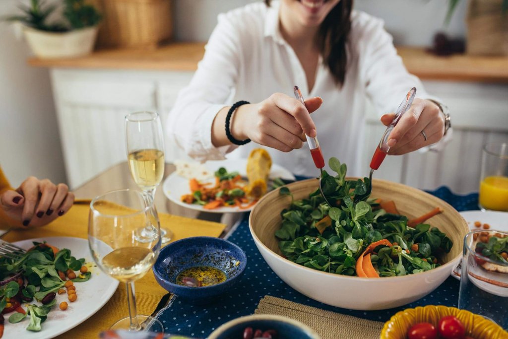 Lachende Frau am Mittagstisch beim Salat-Auftun.