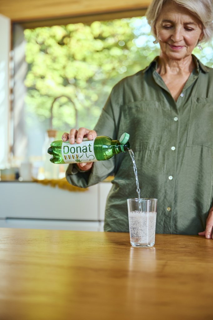 A woman pouring natural mineral water Donat into a glass, which acts against heartburn.