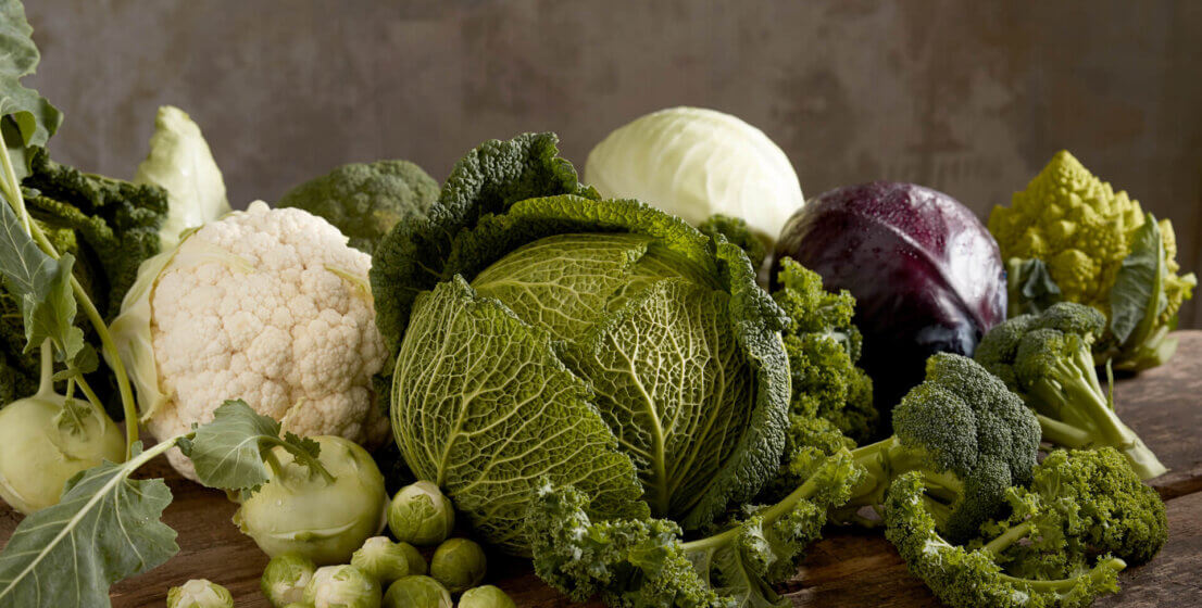 Na drvenom stolu razne vrste svježeg povrća: kelj, cvjetača, prokulice, brokula, korabica i crveni kupus.